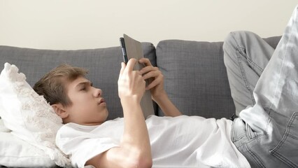 Sleepy tired teenager using digital tablet computer at home. Boy looking at gadget display, touching screen, browsing social media. Internet addiction, bad habits, gadget devices overuse