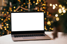 Front View Of White Screen Laptop In Home With Christmas Tree Warm Light. Remote Work. Black Friday Discounts. Online Shopping. Gifts For The New Year And Christmas.