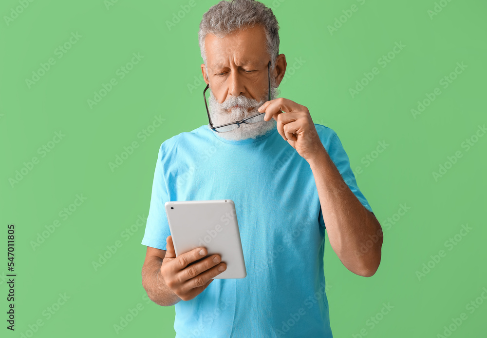 Senior man with eyeglasses using tablet computer on green background