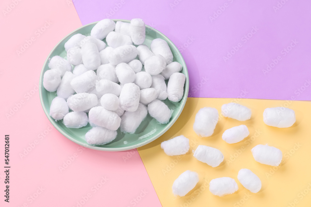 Plate of soft cotton balls on color background
