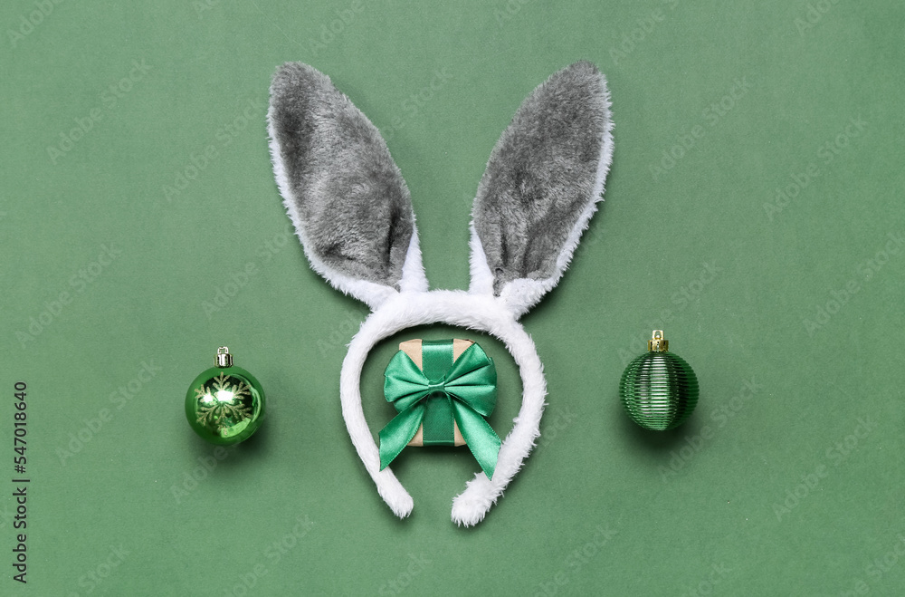 Bunny ears with Christmas balls and gift on green background