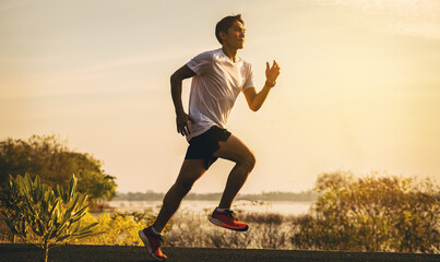 Wall Mural - Silhouette of young man running sprinting on road. Fit runner fitness runner during outdoor workout with sunset background.