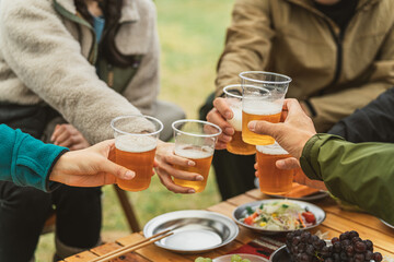 秋冬のキャンプ場で仲間と一緒にビールを飲んでパーティーする男女の手元
