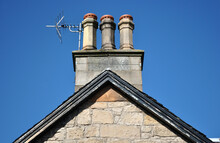 Chimney With TV Antenna On Old Stone Building Seen Against Blue Sky 