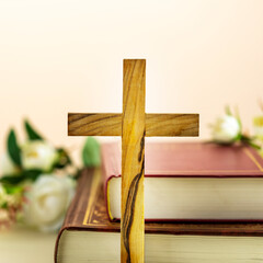 Wall Mural - Religion card with wooden cross with closed red Christian bibles with white flowers on a light gradient background. Easter holiday. Christian religion concept. Front view