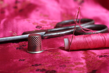 Spool Of Pink Thread And Thimble On Vintage Pink Satin Fabric