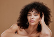 © J Maas/peopleimages.com - Beauty, natural hair and skincare with woman, hair care and wellness cosmetics portrait against brown studio background. Healthy skin, makeup and glow with clean cosmetic mockup and curly hair.