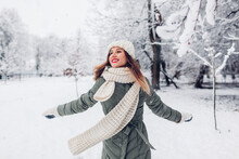 Happy young woman spinning in snowy winter park wearing warm knitted clothes and having fun. Girl enjoying winter