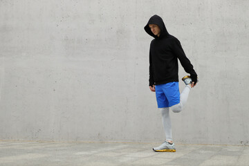 Athletic runner stretching leg and feet and preparing for running outdoors. Active and healthy lifestyle concept. A man in sportswear and a hoodie before running a marathon.