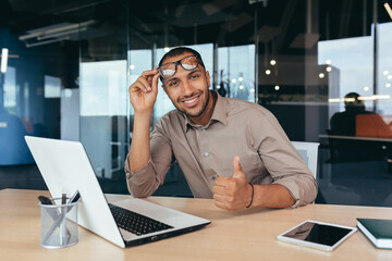 Portrait of programmer in office with laptop African American man looking at camera showing thumb up affirmative.