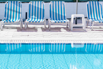  Retro blue and white sunbeds on the poolside of a swimming pool filled with clear blue water at the garden of a holiday resort, travel and tourism concept