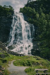 Canvas Print - Vertical and long exposure shot of a waterfall in a valley emerging from the forest in Bergen area