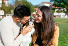 Positive Couple Kissing Dog In Park