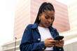 © ADDICTIVE STOCK - Black woman using smartphone on city street