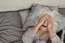 Senior Woman Lying On Bed And Covering Face