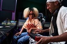 Black Man Playing Synthesizer While Female Watching In Recording Studio