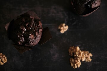 Wall Mural - Top view of a delicious chocolate muffin and walnuts on a dark-colored table