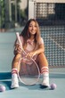 Vertical shot of a young female in pink athleisure posing with a pink racket on a tennis court