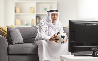 Poster - Arab man in a robe holding a football and watching a match on tv