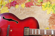 Red electric guitar on a wooden texture background framed by autumn leaves.