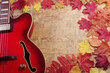 Red electric guitar on a wooden texture background framed by autumn leaves.