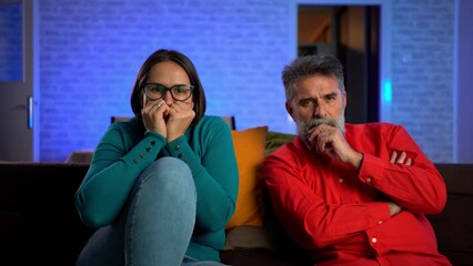 Poster - 4K video footage of a husband and wife watching horror movie in living room. Neon blue light background. good looking Caucasian guy and girl watching interesting film on TV together