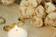 pierścionki, świeczka oraz róże ułożone na starej książce