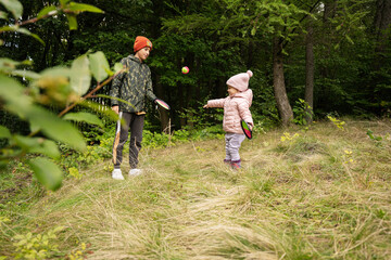 Brother with his little sister play in autumn forest catch and toss ball game.