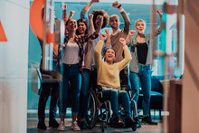 Photo Of Business Women In Wheelchairs With Their Hands Raised In The Air With Their Colleagues, Together Celebrating Business Success