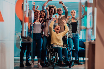 Photo of business women in wheelchairs with their hands raised in the air with their colleagues, together celebrating business success