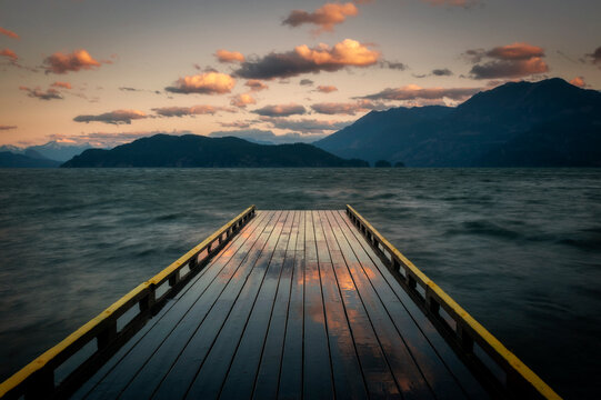 sunrise look at a wooden dock extending out over a lake towards islands and forests. harrison lake i