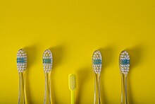 Set Of Identical Toothbrushes Stand As A Group With One Unique Against Yellow Background