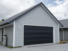 Double Gray Garage With Black Tilt-up Retractable Raised Panel Metal Door And Gable Metal Roof