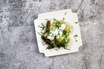 Wall Mural - Stuffed cabbage rolls with meat, rice and sour cream on a white square  plate on a dark background. Top view, flat lay