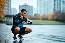 Athletic Man Measuring Heart Rate On Smart Watch While Taking Break Outdoors In Rain.