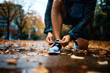 Close up of athletic man tying shoelace while practicing outdoors in rain.