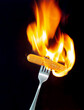 sausage on a fork in fire and black background