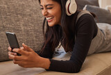 Smartphone, headphones and woman on sofa listening to music, watch online video chat or mobile app zoom call. Excited, relax and music of a youth girl audio, podcast or online subscription streaming