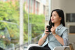 © saltdium - Portrait of Young Asian Businesswoman in formal suit holding a cup of coffee and looking away.