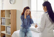 © Studio Romantic - Young Caucasian woman at doctor appointment holding head complaining of headache or migraine looking at therapist writing down symptoms in clipboard sits on medical couch in hospital