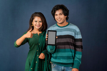 Happy young couple using mobile and showing a blank screen of a smartphone or mobile or tablet phone on a gray background