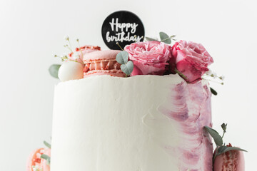 Wall Mural - Birthday cake with white cream cheese frosting decorated with red roses and pink macaroons on the white background. Happy birthday topper on anniversary cake