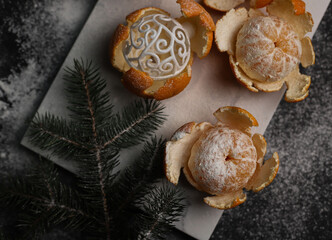 sweet orange juicy tangerines in a peeled peel lie on a black background and a black kitchen tray and in one peel a New Year's ball next to a spruce Christmas branch and sprinkled with white powder.fo