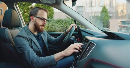 Handsome bearded 25-30-aged modern guy man sitting in front of the handlebar of his own lux class auto and applying navigator.
