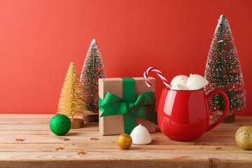 Wall Mural - Christmas hot chocolate cup with marshmallow and Christmas decorations on wooden table over red background