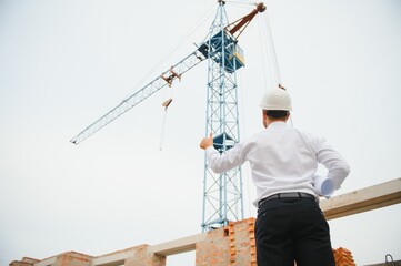 Construction engineer supervising progress of construction project stand on new concrete floor top roof and crane background.