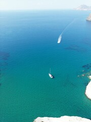 Canvas Print - Bird's eye view of a white boat sailing on crystal-clear blue water near a rocky island