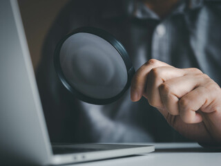 Hand holding magnifying glass for searching or finding information in laptops via online internet computer network. Internet online searching concept.