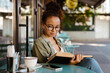 © Drobot Dean - Hispanic woman in eyeglasses drinking coffee and reading book at cafe
