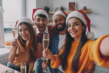 Beautiful People In Christmas Hats Holding Champagne Flutes While Making Selfie At Home